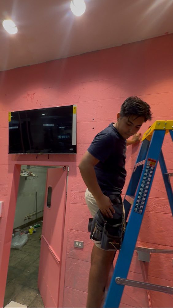 Technician on ladder mounting TV in commercial space